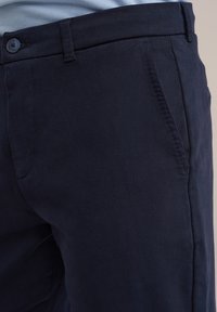 Marineblaue Baumwoll-Chinos mit Knopfverschluss, Seitentaschen und glatter Textur. Merkmale ein gerades Bein-Design mit ordentlicher Naht.