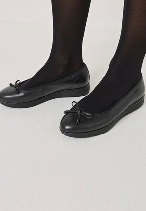 Ballet flats in pelle nera con punta arrotondata, dettaglio di piccolo fiocco e suola in gomma testurizzata. Indossate con collant neri.