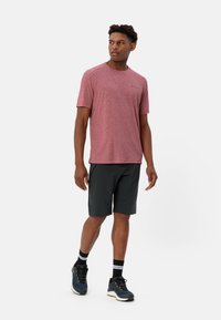 Maglietta sportiva rossa a maniche corte con colletto tondo, abbinata a pantaloni corti scuri. L'outfit presenta un tessuto che allontana l'umidità e una vestibilità ampia.