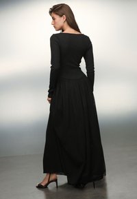 Fekete, hosszú ujjú ruha testes, bordás felső résszel és folyó chiffon szoknyával. Négyzet alakú nyakkivágással és finom csipke díszítéssel a szegélyen.