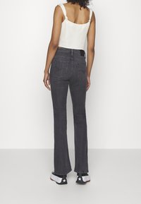 Haut blanc court avec des bretelles nouées, associé à un jean flair gris foncé et des baskets noir et blanc avec des accents étoilés.