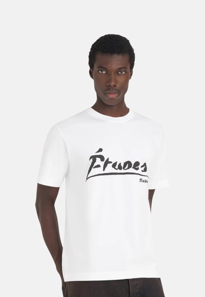 T-shirt en coton blanc à manches courtes, avec un imprimé graphique noir "Étrudes" sur le devant. Encolure ronde classique.