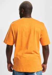 Oransje bomulls-T-skjorte med en avslappet passform, korte ermer og et merke på venstre side. Glatt tekstur og enkelt design.