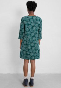 Teal dress with floral pattern, three-quarter sleeves, round neckline, and a relaxed fit, paired with navy ankle boots and cream socks.