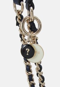 Smycz łańcuszkowa z metalowymi ogniwami w złotym odcieniu i elementem ze granatowej skóry. Dwie okrągłe zawieszki: jedna czarna z znakiem zapytania, druga biała z tłoczonym tekstem.