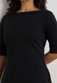 Czarna, dopasowana sukienka z dekoltem typu łódka i krótkimi rękawami. Gładka tkanina o lekkim połysku, dopasowany krój podkreślający sylwetkę.