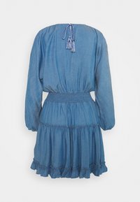 Denimmekko, jossa on pitkät puff-hihat, smokkautuva vyötärö ja kerroksellinen röyhelöhelma. Vaaleansininen kangas, jossa on takana solmittava nauha, joka sisältää tupsut.