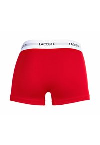 Czerwone bawełniane szorty z białym paskiem w talii, na którym znajduje się logo Lacoste. Projekt charakteryzuje się gładką teksturą oraz średnim stanem.