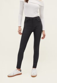 Jean skinny taille haute noirs avec poches avant, associés à un top blanc à épaules dénudées et des baskets blanches avec des accents gris.