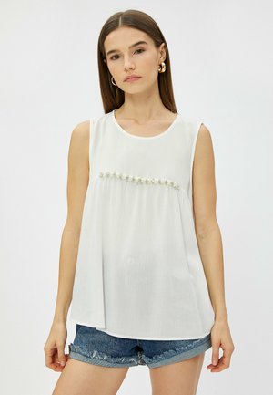 Witte mouwloze blouse met een ronde halslijn, voorzien van een textuurstof en een decoratieve rij kleine bloemen bij de buste.