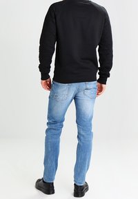 Černá mikina s prošívanými rukávy, zkombinovaná se světle modrými džíny. Doplněna černými botami. Zaměření na zadní pohled.