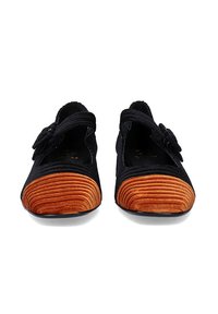 Zapatos de tela negros con puntera naranja estriada, que cuentan con una correa y un lazo decorativo en el costado. Diseño de suela plana adecuado para uso casual.