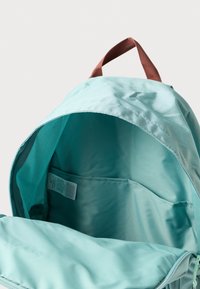 Türkizkék hátizsák barna szövet fogantyúval, tágas belső térrel és hálós zsebbel. Egységesen sima, szintetikus anyagú felület.