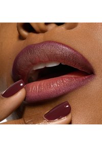 Rouge à lèvres bordeaux mat appliqué sur les lèvres, mettant en valeur un effet dégradé. Ongles bordeaux brillants touchant les lèvres, soulignant la texture lisse.