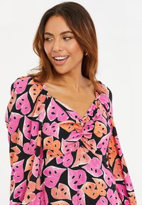 Kukallinen mekko V-pääntiellä, jossa on musta tausta ja suuria pinkkejä ja oransseja lehtikuvioita; pehmeä kangas ja rento istuvuus.