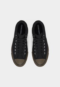 Mustad madalavärvilised Converse tennised, millel on pruunid kummist ninaosad ja tallad, mustad paelad ning nähtav "CONVERSE" logo sisemisel küljel.