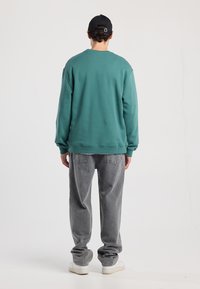 Teal sweatshirt with crew neck and cuffed sleeves, paired with loose-fitting gray jeans and white sneakers. Plain design, no visible patterns.