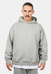 Hoodie vaaleanharmaasta pehmeästä kankaasta, jossa on kengurupocket, säädettävä nyörihuppu sekä ribbailevat hihat ja helma.