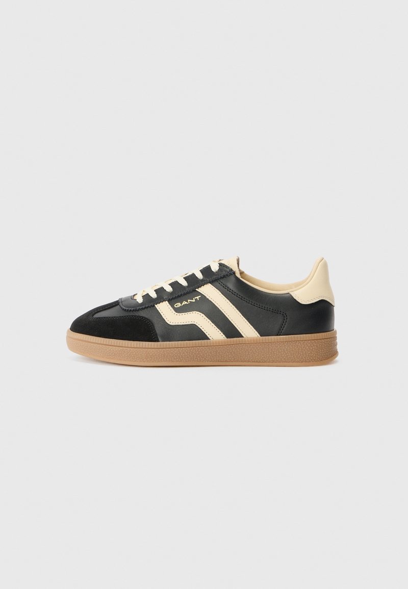 Baskets basses noires et beiges avec semelle en gomme, lacets crème et logo GANT sur le côté, présentées de profil sur fond uni.
