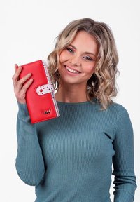 Red wallet with a polka dot pattern on the inside and a snap closure, featuring a metallic logo accent on the front.