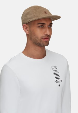 Casquette en velours côtelé beige avec un patch en bois. Chemise à manches longues blanche avec un texte noir et des détails graphiques sur le devant.