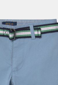 Ljusblå byxor med ett vävt marinblått bälte som har gröna och rosa ränder. Lappen säger "POLO." Tvättbart tyg med slät textur.