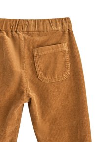 Bruine corduroy broek met een gestructureerde afwerking, voorzien van een elastische tailleband en een enkele achterzak. Verticaal ribbelpatroon zichtbaar.