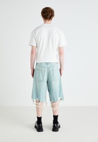 Tricou alb cu mânecă scurtă, asortat cu pantaloni scurți din denim albastru deschis, deteriorați, având margine desfăcută și două buzunare pe spate, purtat cu încălțări negre.