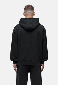 Felpa nera con cappuccio, dal taglio rilassato, in tessuto testurizzato e con polsini a costine. Presenta una tasca a marsupio e un design in tinta unita.