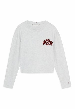 Jasnoszara, długorękawowa, krótkia koszulka z okrągłym dekoltem, z bordowym herbem z dwoma lwami na lewej piersi oraz małą flagą na rękawie.