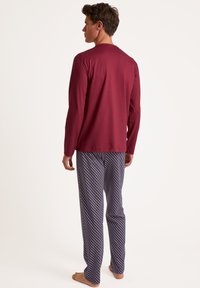 Chemise rouge à manches longues avec un col rond, associée à un pantalon de pyjama bleu à motifs comportant des losanges rouges et blancs.