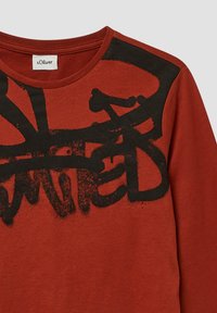 Gebrandoranje langwerpige shirt gemaakt van katoen, met een zwart abstract grafisch print op de bovenste linkerzijde. Ronde halslijn, ribbelstructuur.