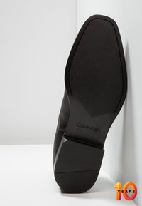 Černá kožená podrážka s texturovaným designem a embosovaným logem "Calvin Klein". Pevný tvar, hladký povrch a minimalistické detaily.