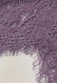 Lila Spitzenstoff mit floralen Mustern, kunstvollen Details und einer fransigen Kante, der eine weiche, strukturierte Optik aufweist.