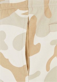 Shorts de camouflage beige en coton doux, avec une coupe décontractée et une poche arrière. Le motif comprend des formes beige claires et foncées.