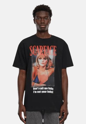 T-shirt in cotone nero con una stampa grafica di una donna in bikini blu, accompagnata da un audace testo rosso "SCARFACE" e uno slogan in basso.