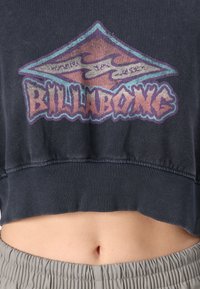 Rövidített sötétkék pulóver, amely színes grafikai mintával rendelkezik, a "BILLABONG" felirattal az elején és bordázott aljjal.