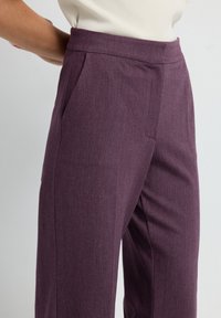 Pantalons taillés violets avec une texture lisse, dotés de poches latérales et d'un design à jambe droite. Taille plate à l'avant.