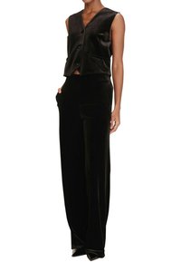 Gilet corto in velluto nero con scollo a V e tre bottoni, abbinato a pantaloni a vita alta con gamba ampia e tasche laterali.