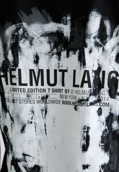 Fekete és szürke grafikus póló, absztrakt ecsetvonás mintákkal. Tartalmazza a márka logóját és szöveget vastag fekete betűtípussal.