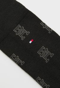 Schwarze Socken mit grauen geometrischen Logo-Mustern und einem kleinen roten, weißen und blauen Logo-Akzent in der Mitte.