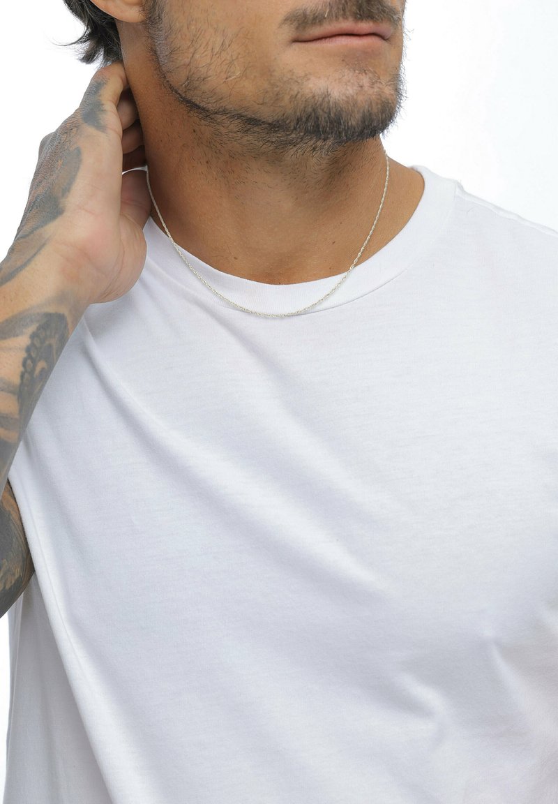 Sølv kædehalskæde båret over en enkelt hvid t-shirt. T-shirten har rund halsudskæring og en glat, blød tekstur.