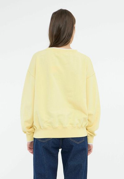 Gul sweatshirts med en afslappet pasform, sænkede skuldre og ribbet kant. Sammen med mørke denim jeans. Glat bomuldsstruktur.