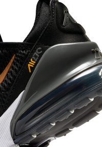 Κοντινό πλάνο της φτέρνας μαύρου αθλητικού παπουτσιού Nike Air 270 με υφασμάτινο πλέγμα, πορτοκαλί σήμα και διαφανές μαξιλαράκι στη σόλα.