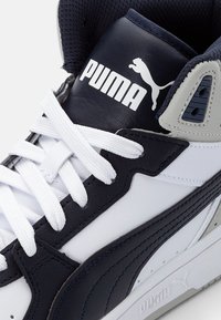 Vit och marinblå sneaker med läder- och meshmaterial, texturerade detaljer, framträdande Puma-logotyp och vita skosnören med vadderad hals.
