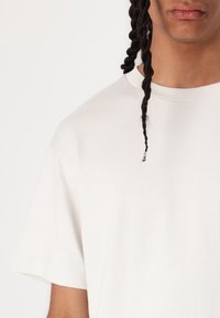 Witte korte mouwen t-shirt van katoen; ronde halslijn met ribbelrand; zachte textuur met minimale details; lichte rafeling aan de zoom.