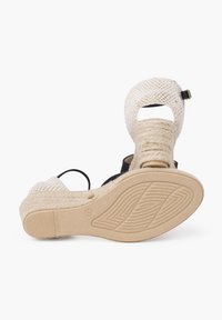 Wedge sandals with woven beige fabric, an open toe design, and black strap accents; textured jute detailing on the sole with a rubber base.
