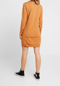 Robe orange à manches longues avec une coupe décontractée, dotée d'un ourlet arrondi et d'une poche latérale, associée à des baskets montantes noires.