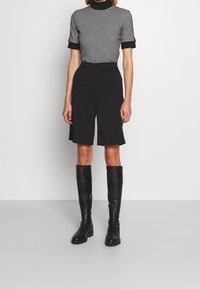 Czarno-biała bluzka w wzór houndstooth z krótkim rękawem, czarne dopasowane szorty oraz czarne skórzane kozaki do kolan na płaskiej podeszwie.