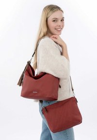 Červená měkká kožená hobo taška s uvolněným designem, obsahující odnímatelný popruh a malou odpovídající tašku přes rameno se zipovým uzávěrem.